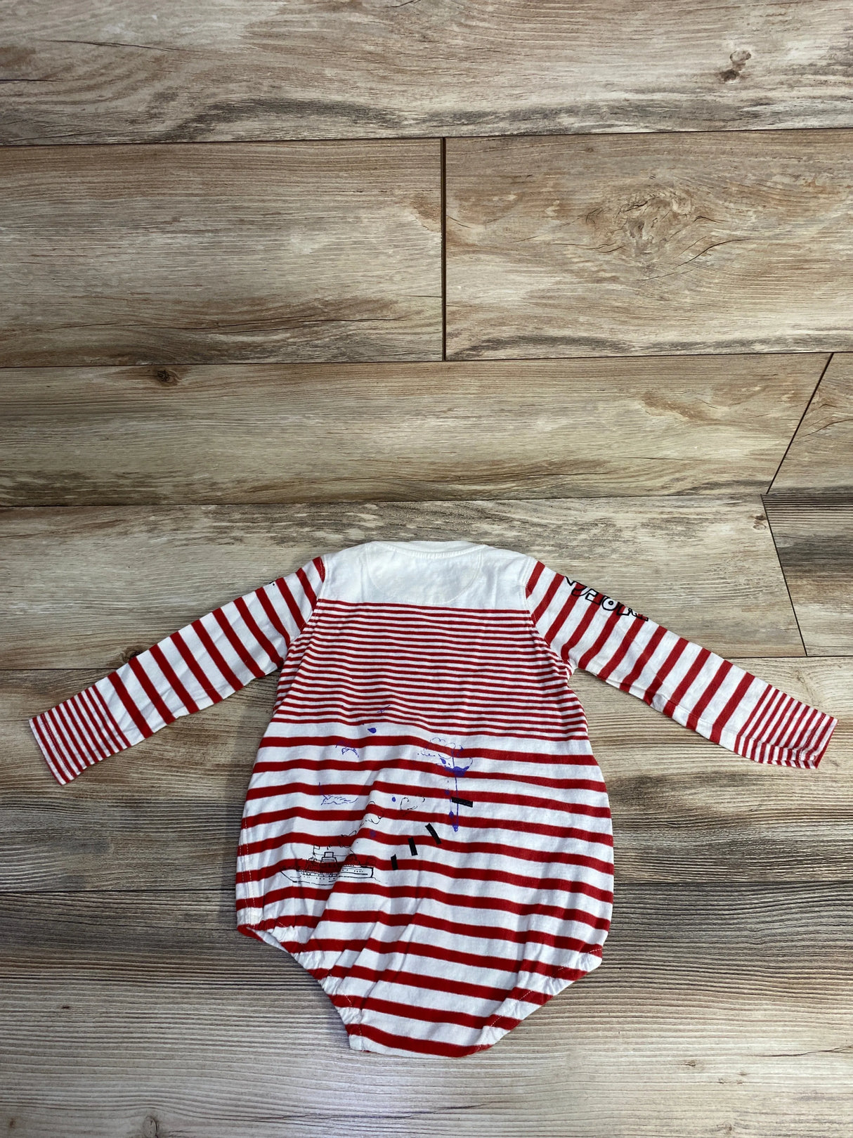 Red and white striped long-sleeve baby onesie with nautical print on wooden floor