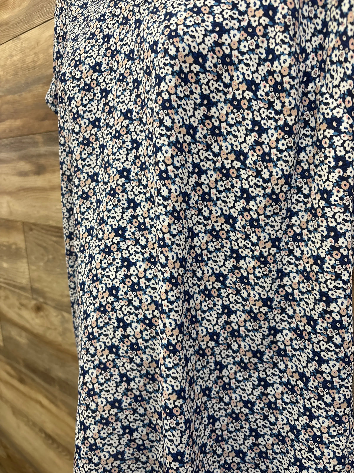 Close-up of Motherhood Maternity shirt showcasing blue fabric with dense white and pink floral print on a wood floor