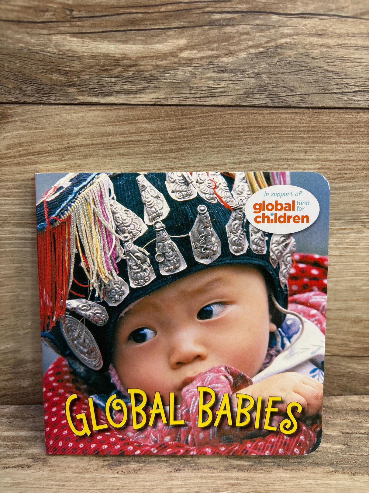 Baby wearing traditional ethnic headwear with silver ornaments on book cover titled Global Babies