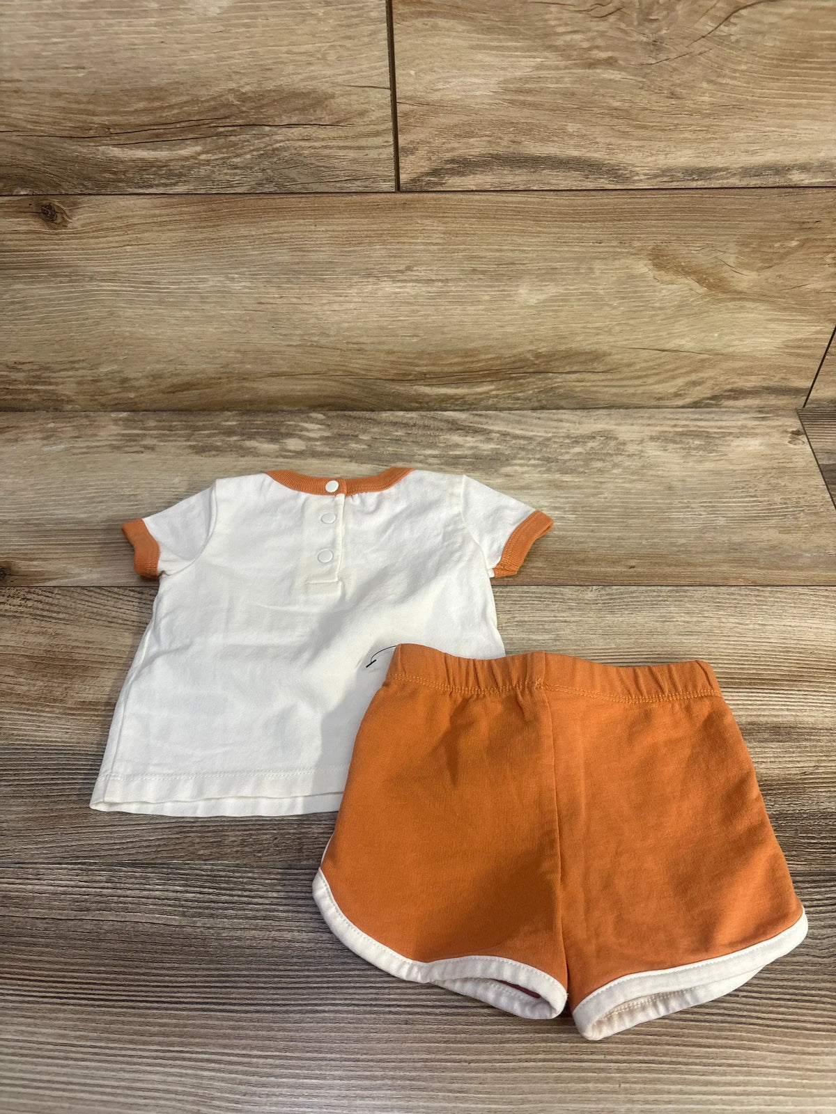 Flat lay of Focus sun shirt and shorts set, white shirt with orange trim and orange shorts on wood flooring