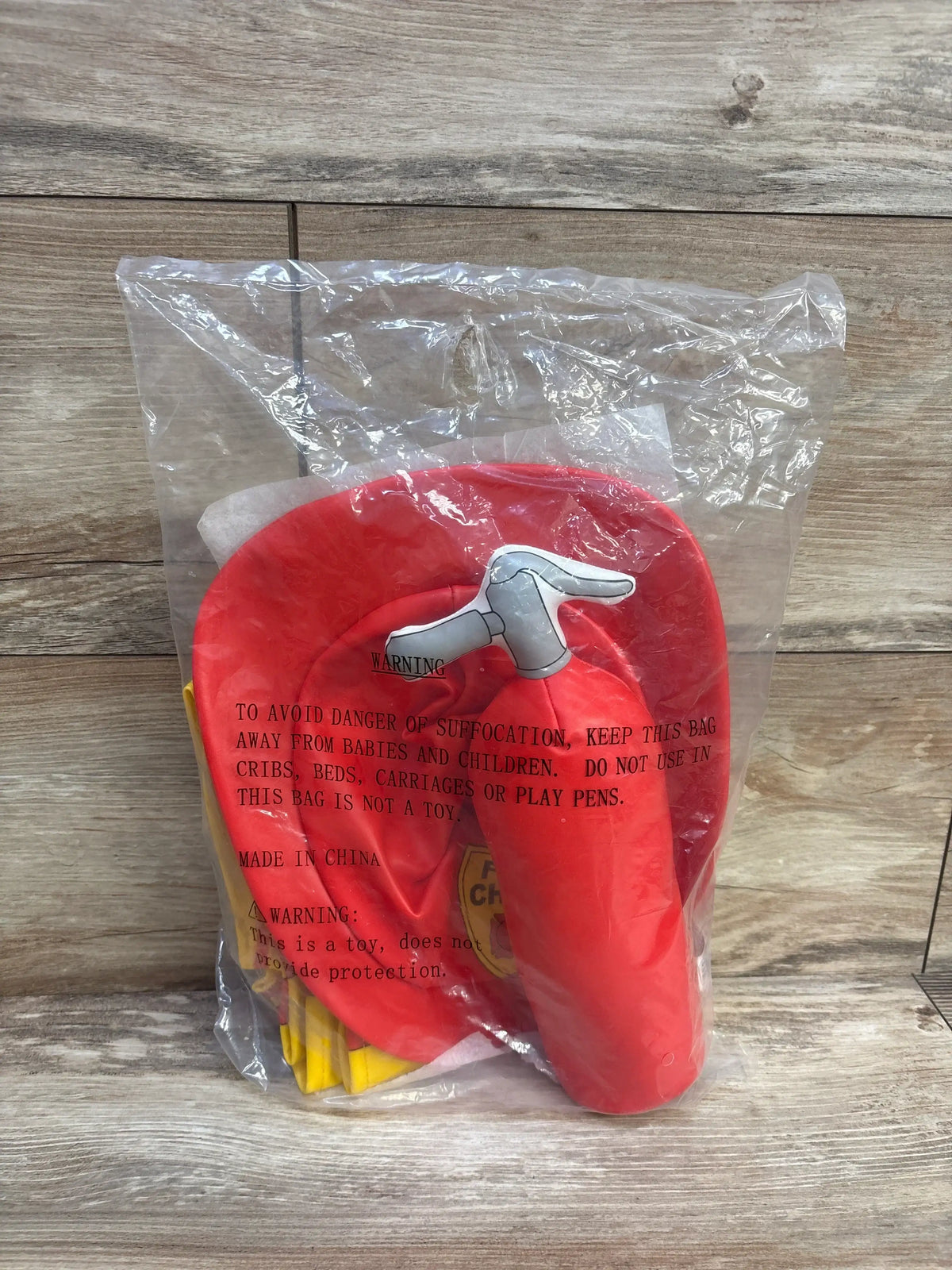 Front view of Lakeshore toddler firefighter costume showing a red firefighter helmet and yellow costume pieces in clear packaging