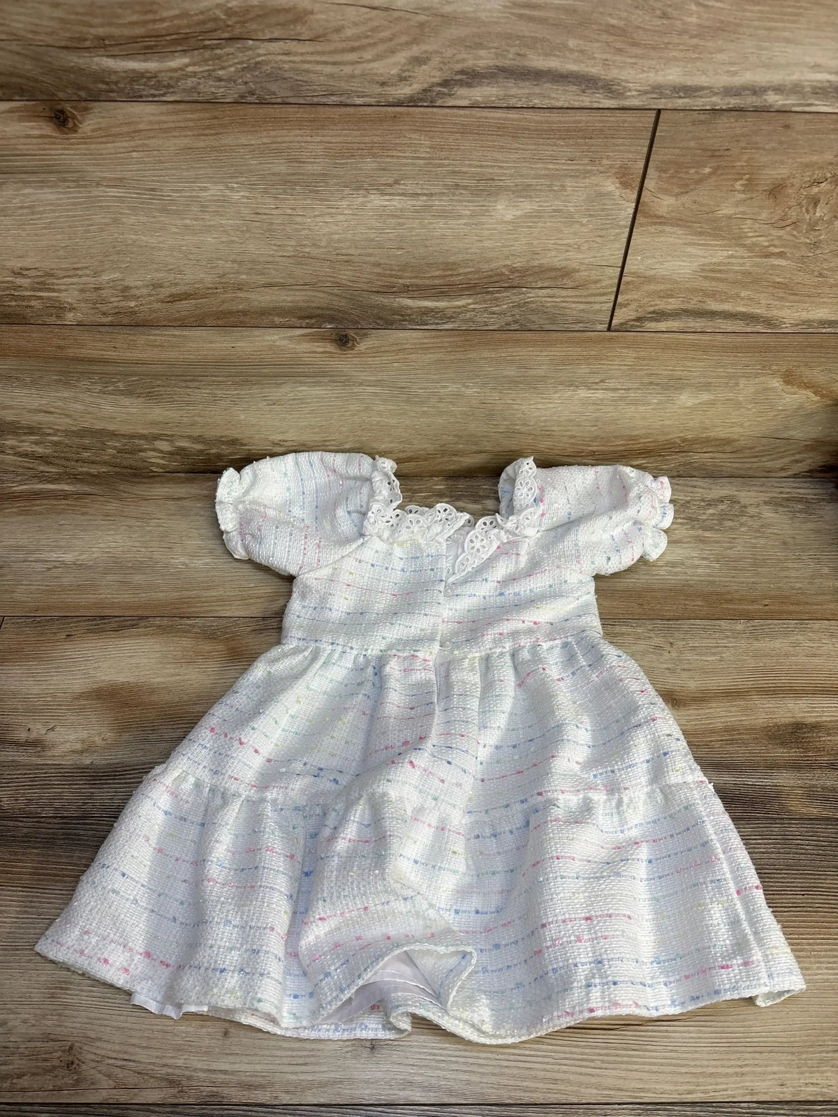 White baby dress with pastel stripes, lace trim, and puffed sleeves on wood floor