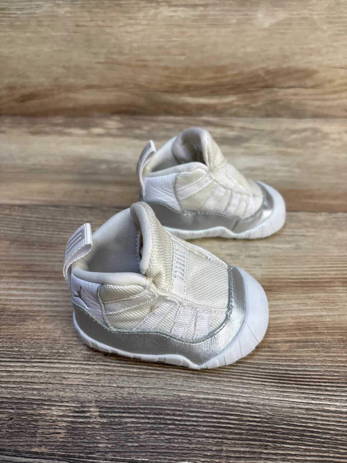 Three-quarter view of Air Jordan 11 Retro TD 'Metallic Silver' toddler sneakers showing white mesh upper and silver mudguard on wood surface