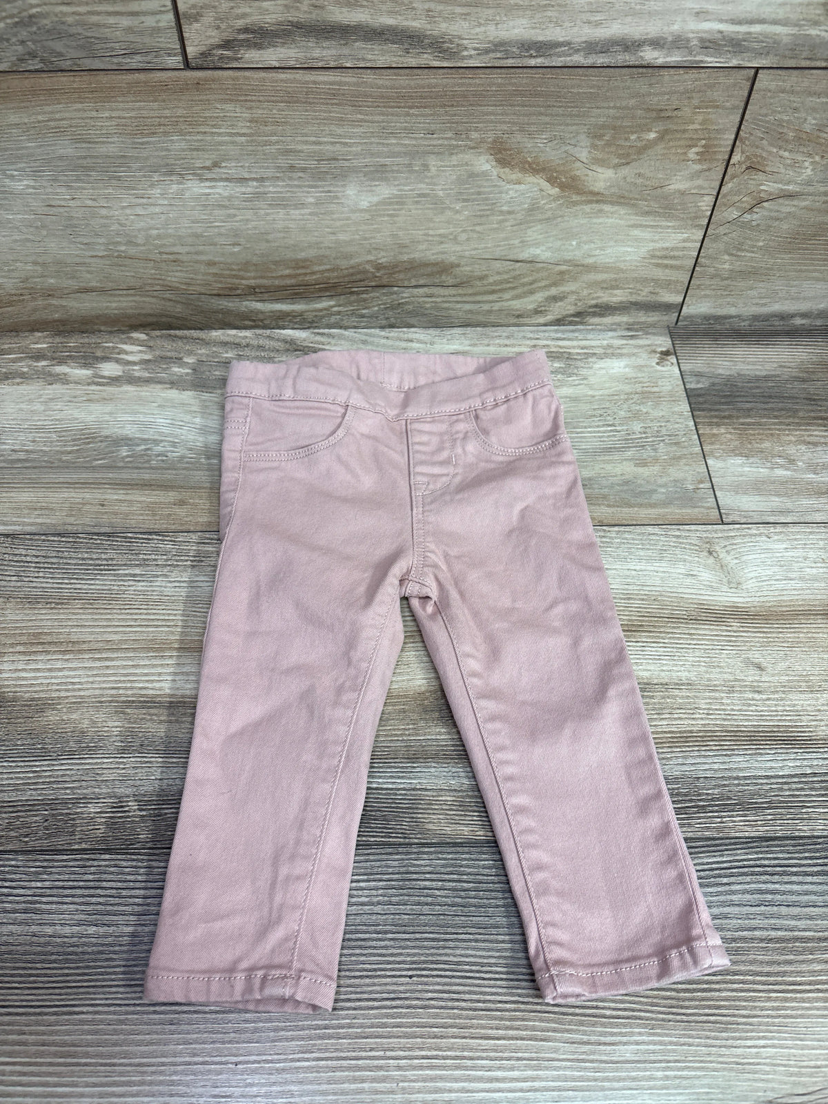 Front view of H&M pull-on pants in pink, size 9 months, with an elastic waist and front pockets on a wood-look floor