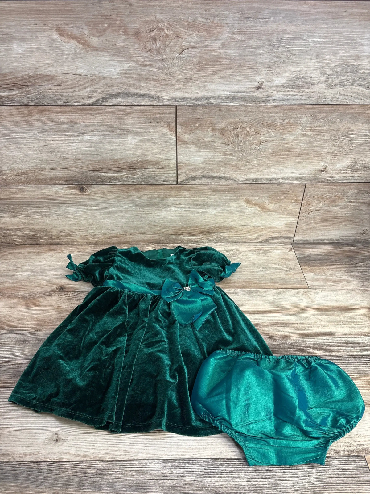 Green velvet baby dress with bow and matching bloomers on wooden background