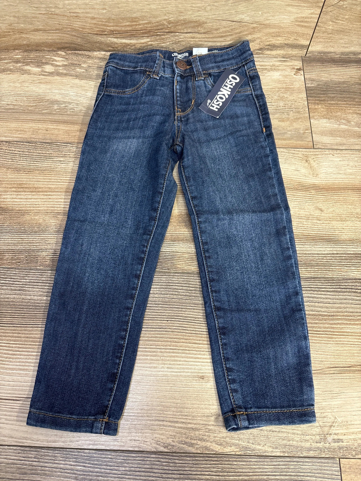 Dark wash kids' jeans with OshKosh tag, front view on wood floor