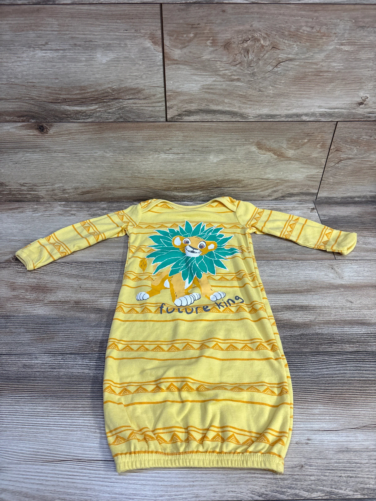 Flat lay of yellow Disney Baby Lion King sleep gown showcasing lion graphic and elastic bottom on wood backdrop