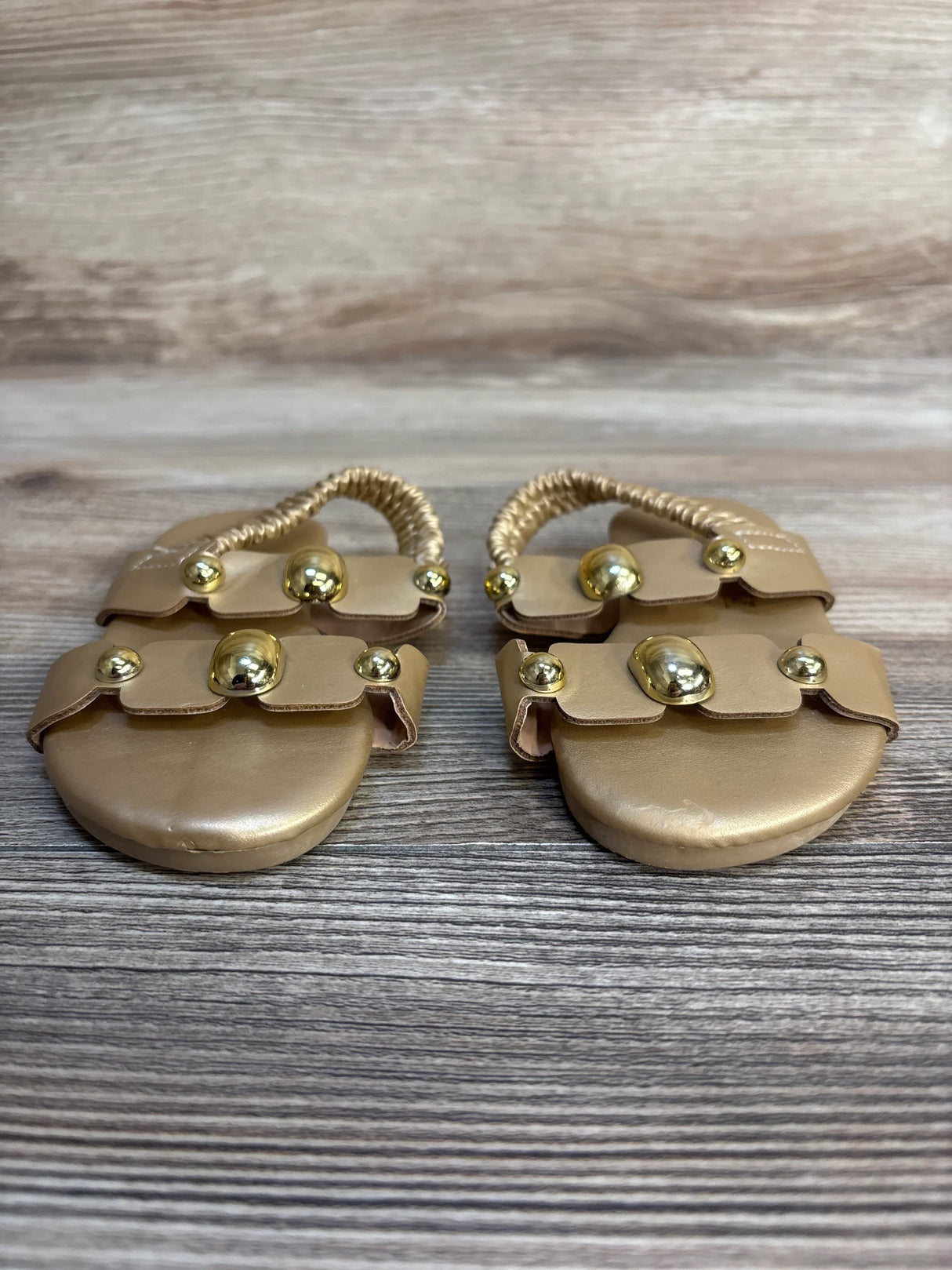 Gold baby sandals with metallic studs on a wood background, children's footwear