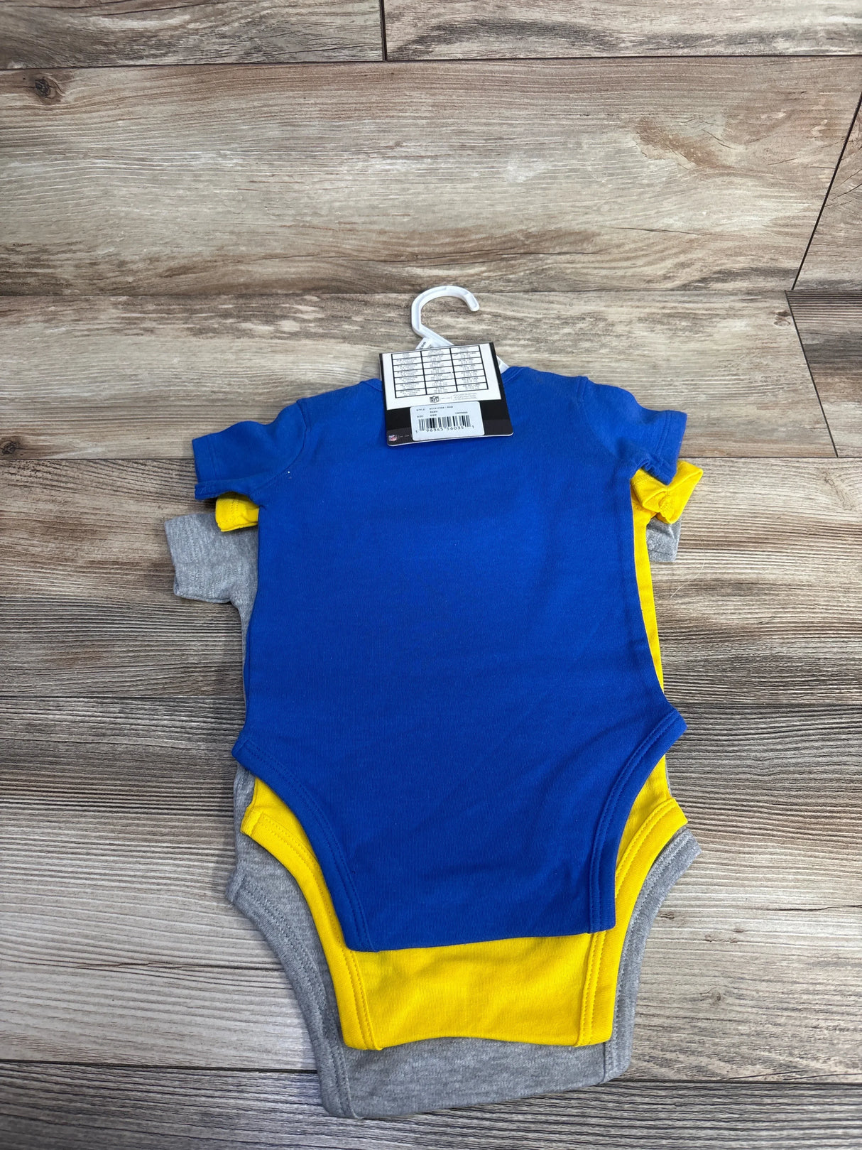Top view of 3-pack Los Angeles Rams baby creepers in blue, yellow and gray showing short sleeves and snap crotch on wood floor