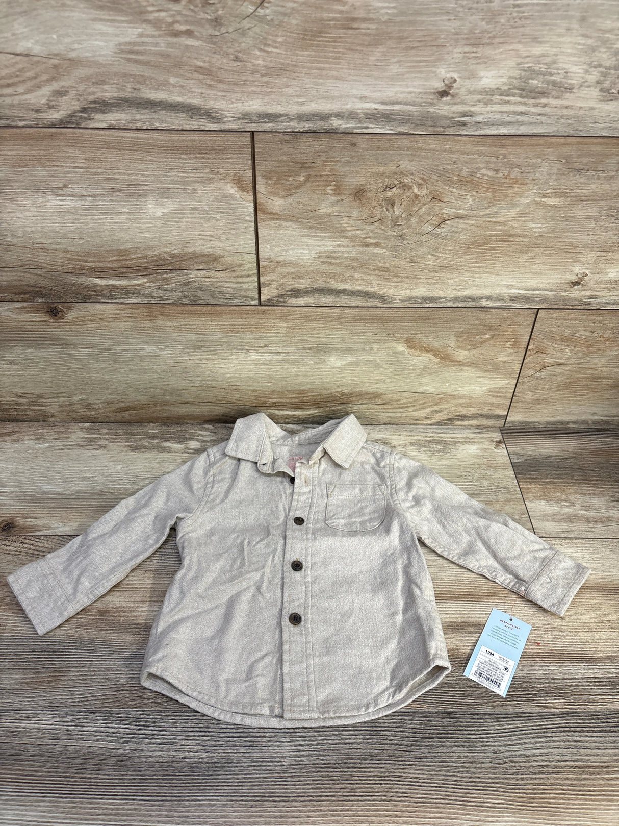 Flat lay of beige Cat and Jack 12M button-up shirt showing front buttons, chest pocket, and long sleeves on wood background