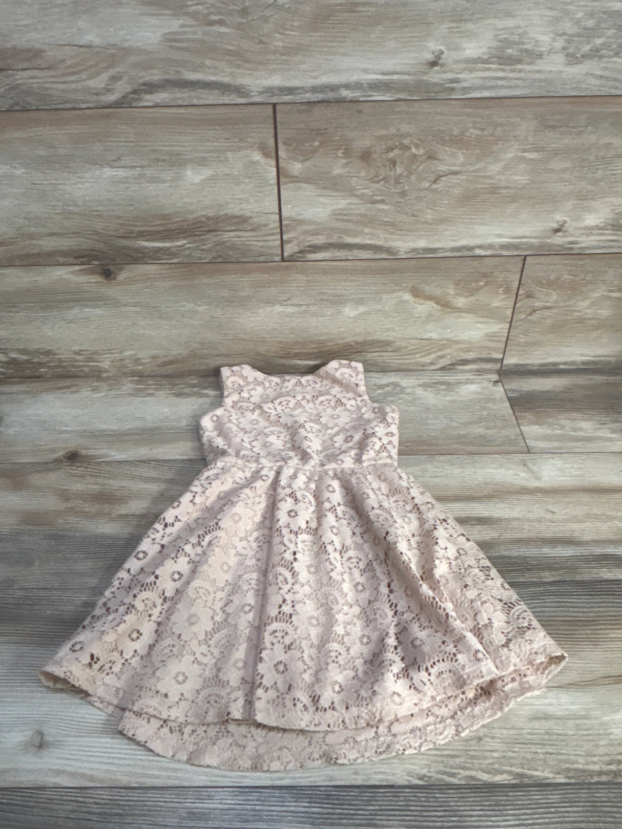 Flat lay of Lily Bleu girls' lace dress showcasing floral lace overlay and high-low scalloped hem with light wood floor background