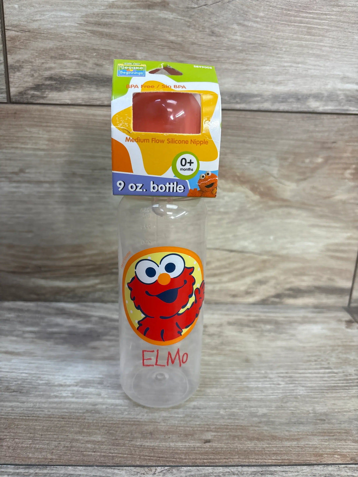 Front view of Sesame Street Beginning 9oz bottle showcasing Elmo design and medium flow silicone nipple packaging on a wood surface