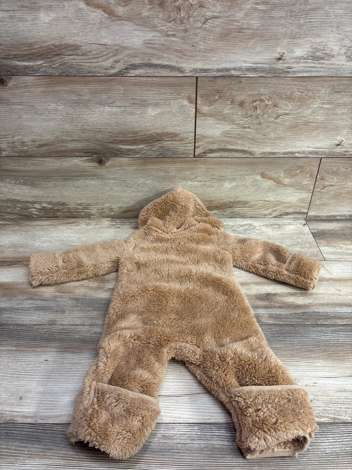 Tan Nike sherpa hooded baby coverall laid flat on a rustic wooden background.