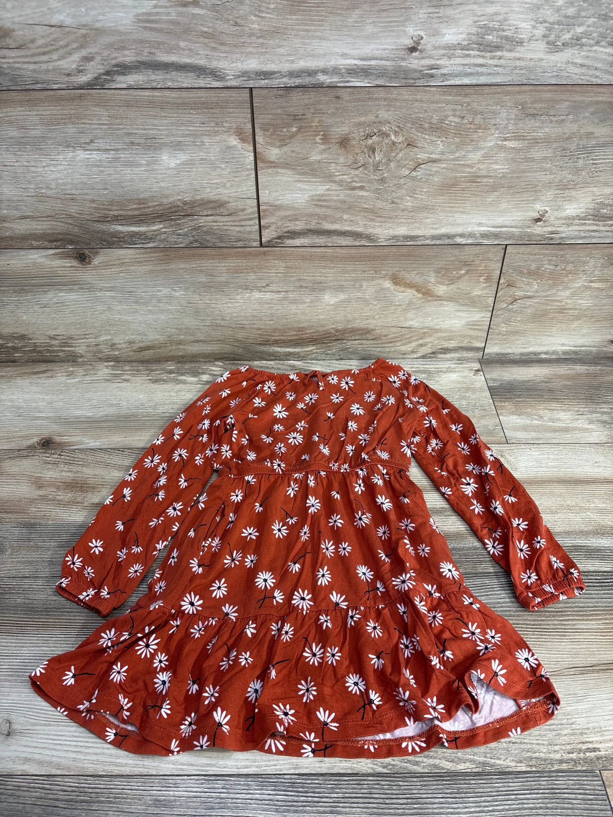 Rust orange long-sleeve toddler dress with white daisy flower pattern on wood floor