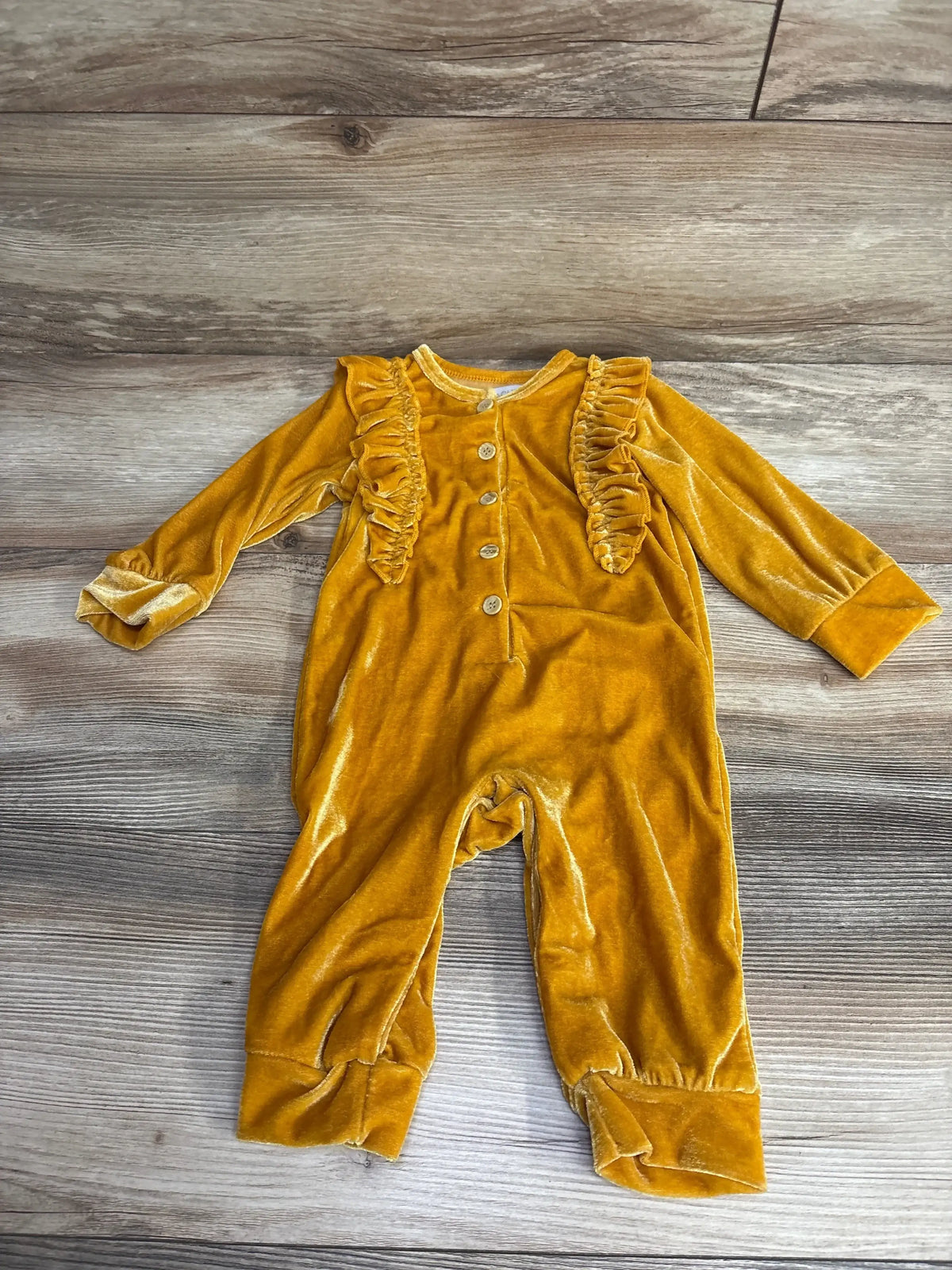 Yellow velvet baby romper with long sleeves, ruffle details, and buttons on wood floor