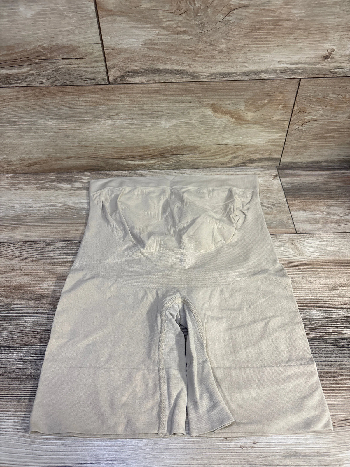 Front view of beige seamless maternity shapewear shorts showcasing high-waisted coverage on a wood-look floor