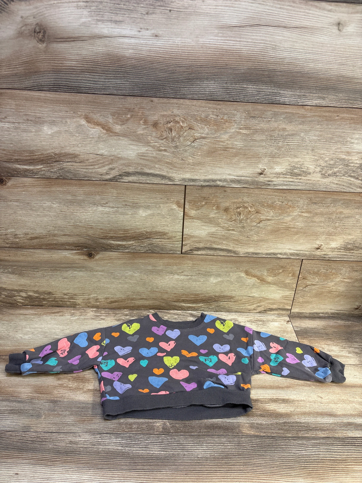 Front view of Mud Kingdom heart-print toddler sweatshirt showcasing multicolor hearts on grey fabric with wood plank background