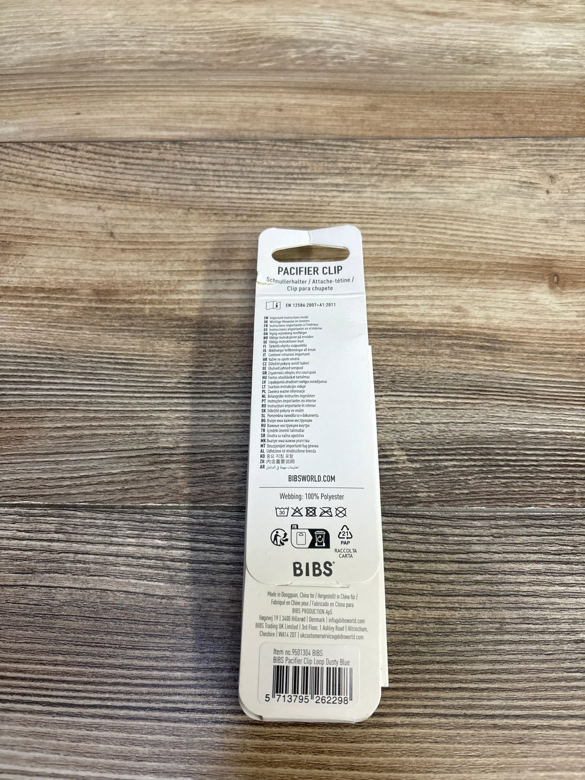 Back view of BIBS pacifier clip packaging showing product information, care symbols, and barcode on a wood table