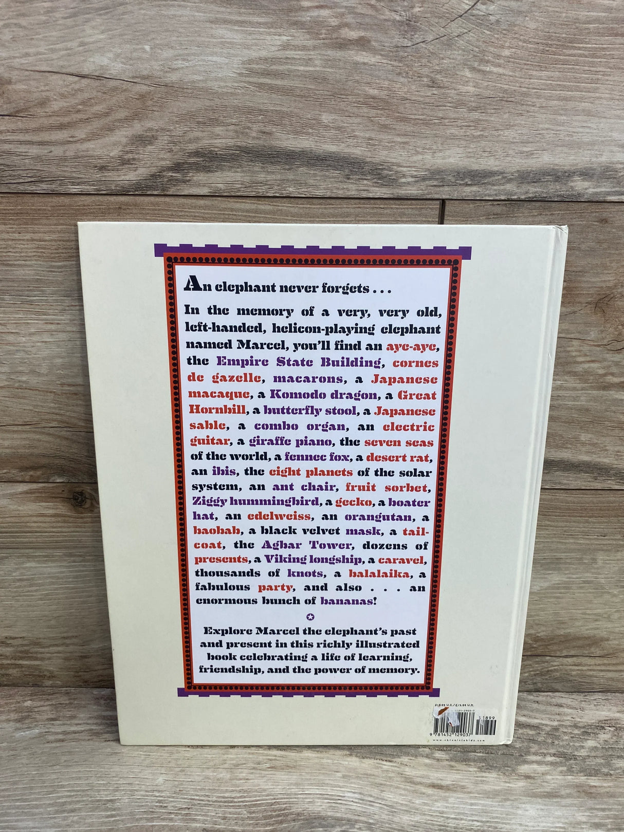 Back cover of a book with a text block describing Marcel the elephant's memories, on wooden surface