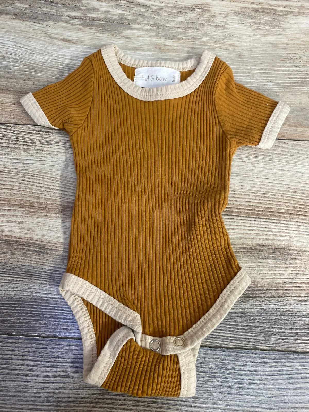 Ribbed mustard yellow baby onesie with beige trim and snaps on wooden floor