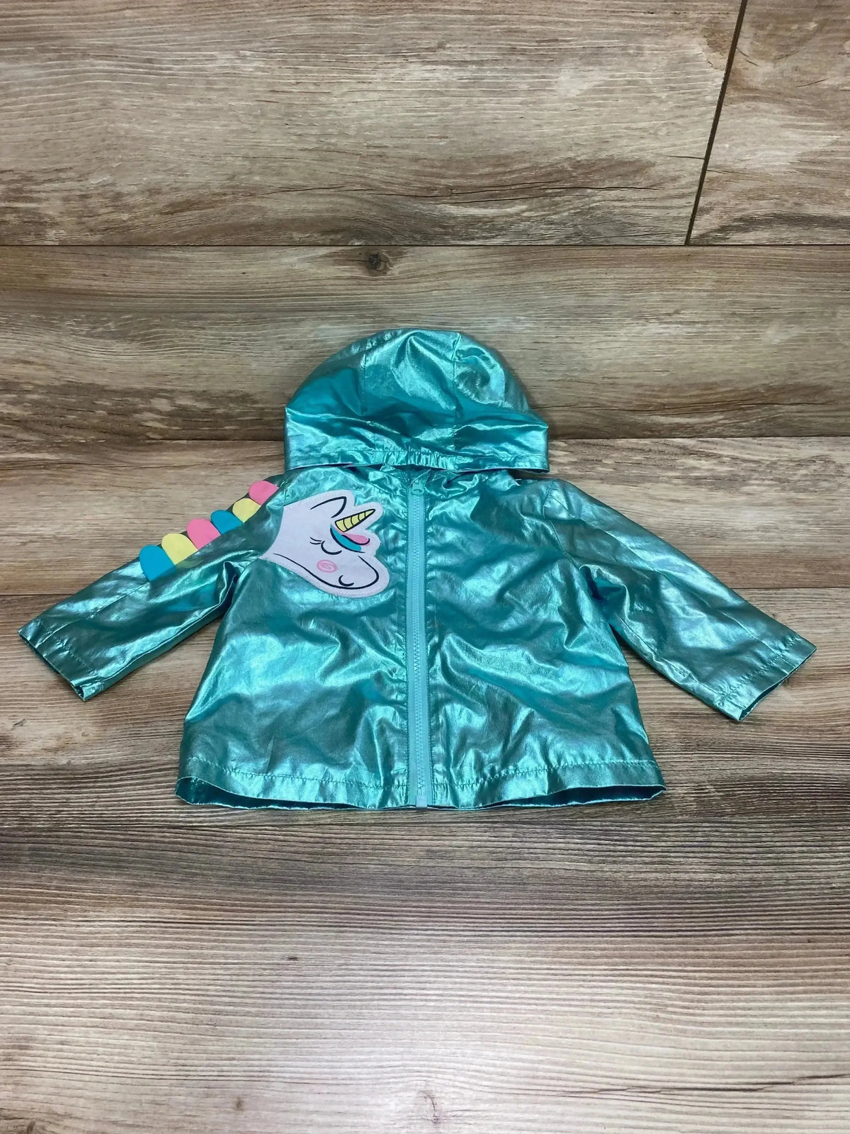 Front flat-lay of Wonder Nation unicorn windbreaker in metallic teal with hood, center zipper, and unicorn applique on wood