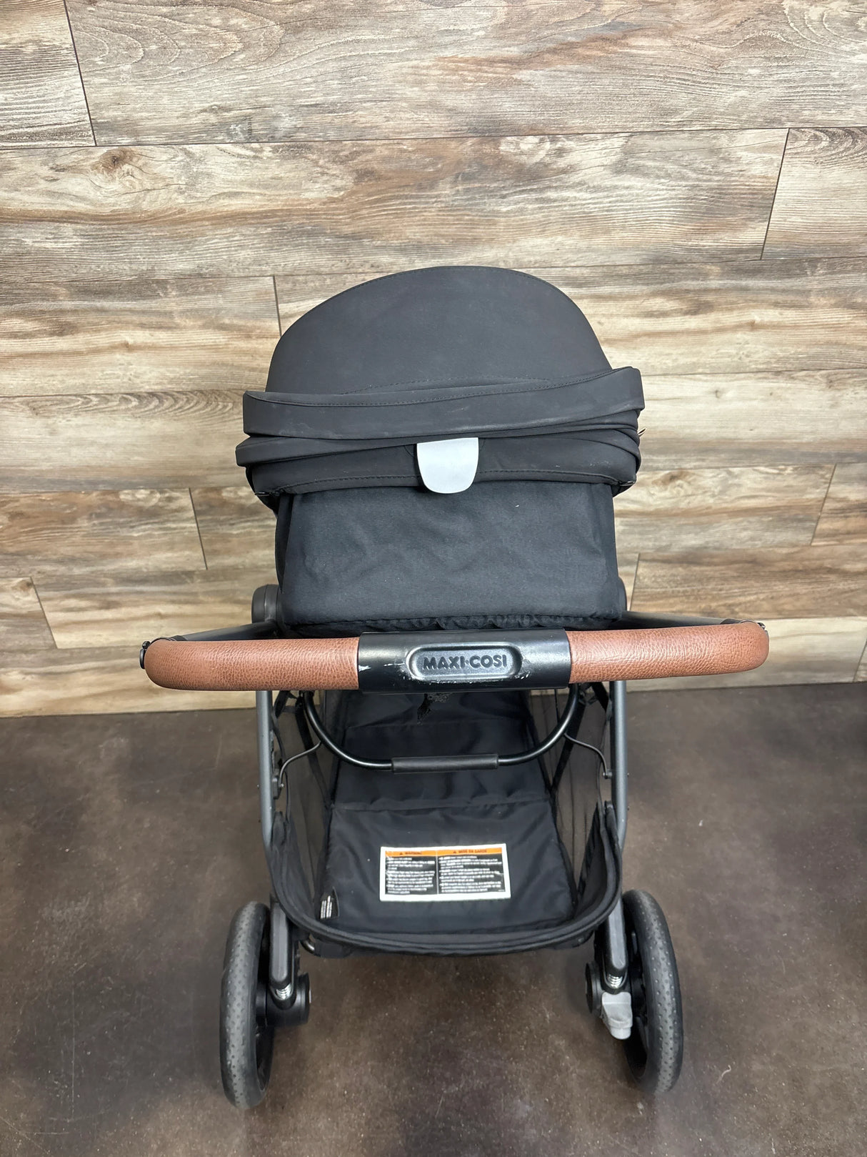 Maxi-Cosi black baby stroller with brown handle, indoor wood background