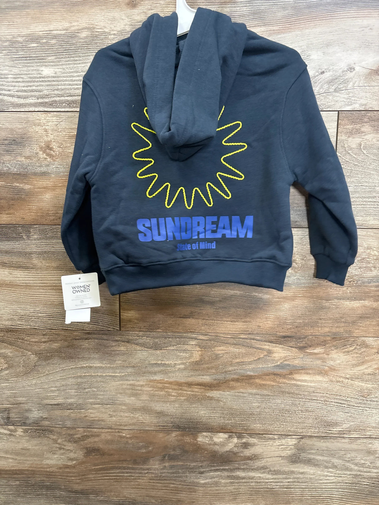 Back view of navy toddler pullover hoodie showcasing yellow sun embroidery and blue SUNDREAM text with wood-plank background