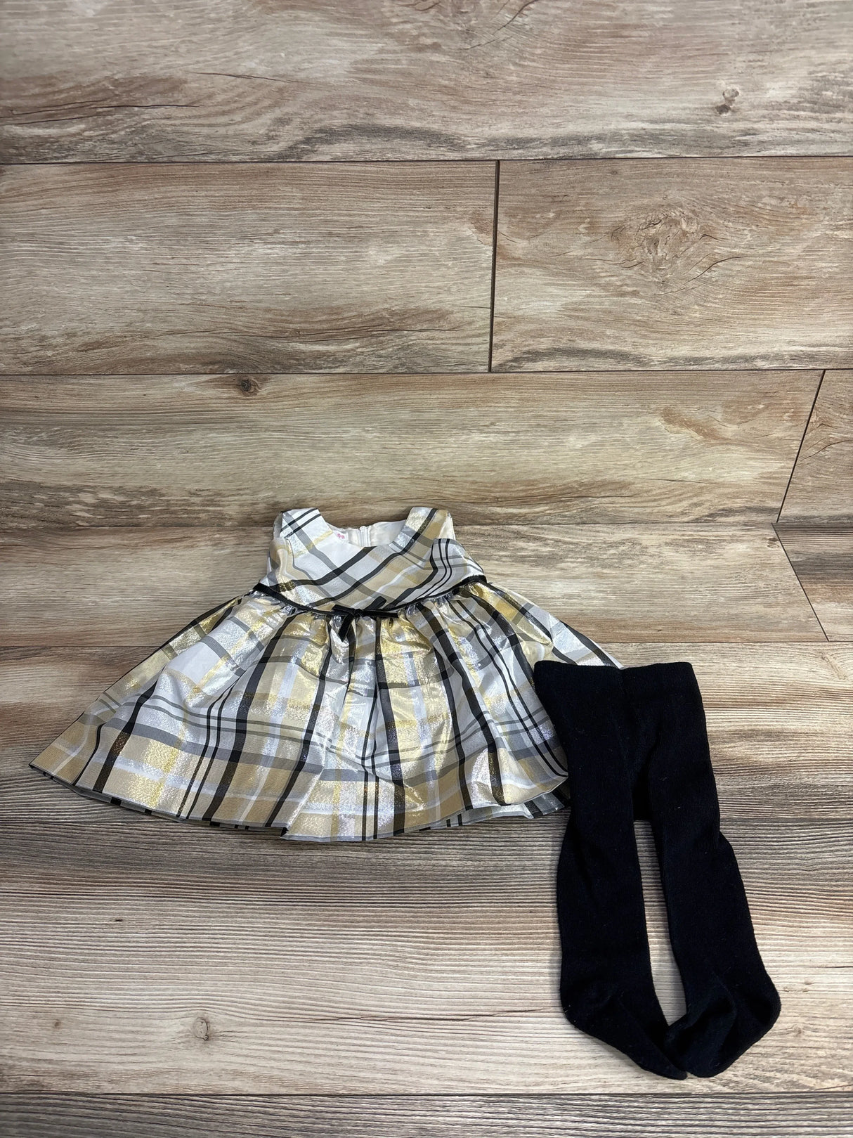 Plaid baby dress with gold, black, and white pattern paired with black tights on wood floor