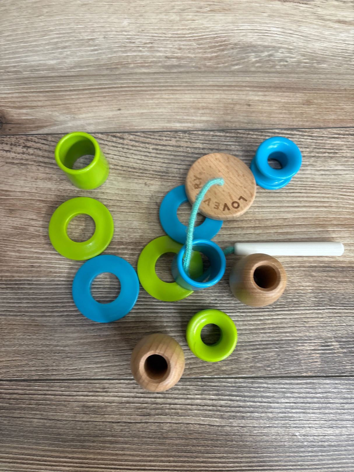 Wooden toddler lacing toy with green and blue rings on a wood surface