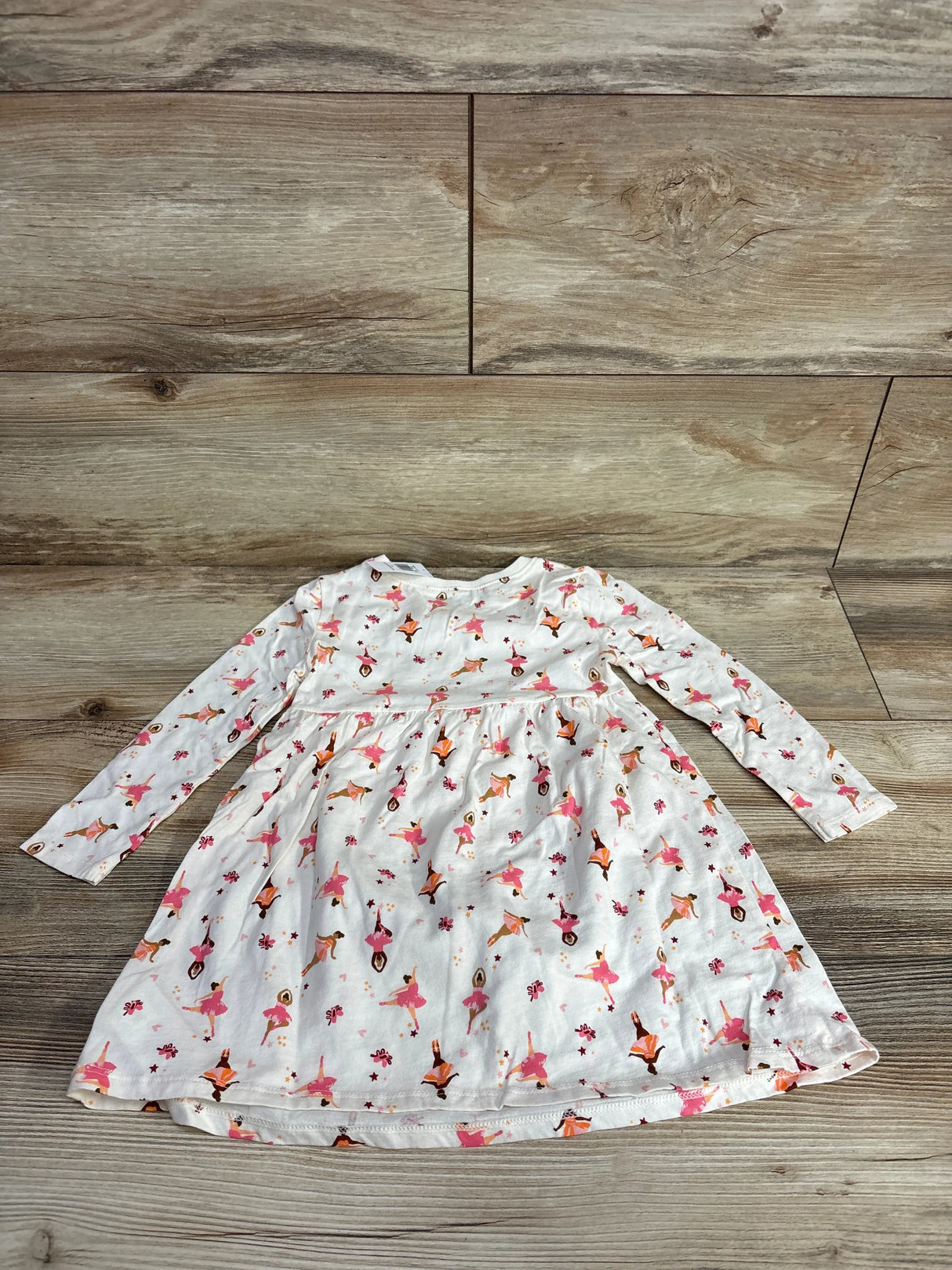 Long-sleeve toddler dress with pink and orange ballerina print on white fabric, laid on wooden floor