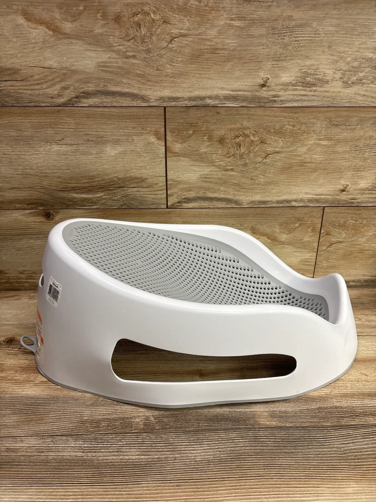 Side view of Angelcare Bath Support showcasing its perforated grey reclining seat with a wood plank background