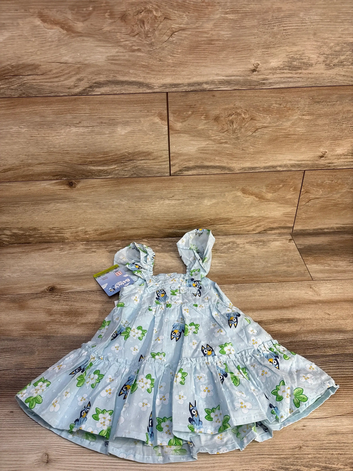 Flat lay of light blue 12M toddler dress with Swiss-dot, ruffled straps, tiered skirt and Bluey floral print on wood