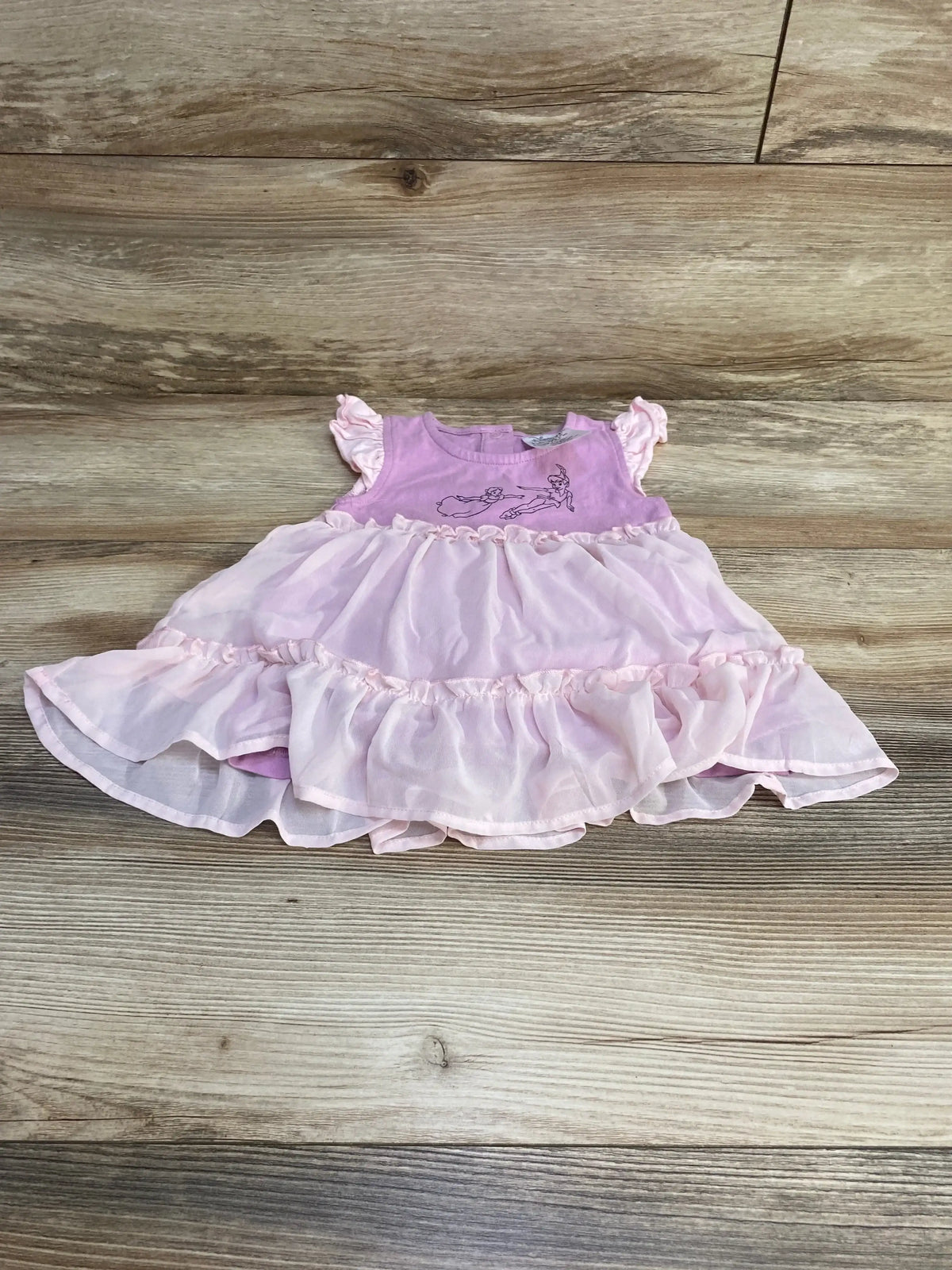 Flat lay of purple Disney baby dress with layered chiffon skirt and Peter Pan and Wendy print, plus matching bloomers on wood background