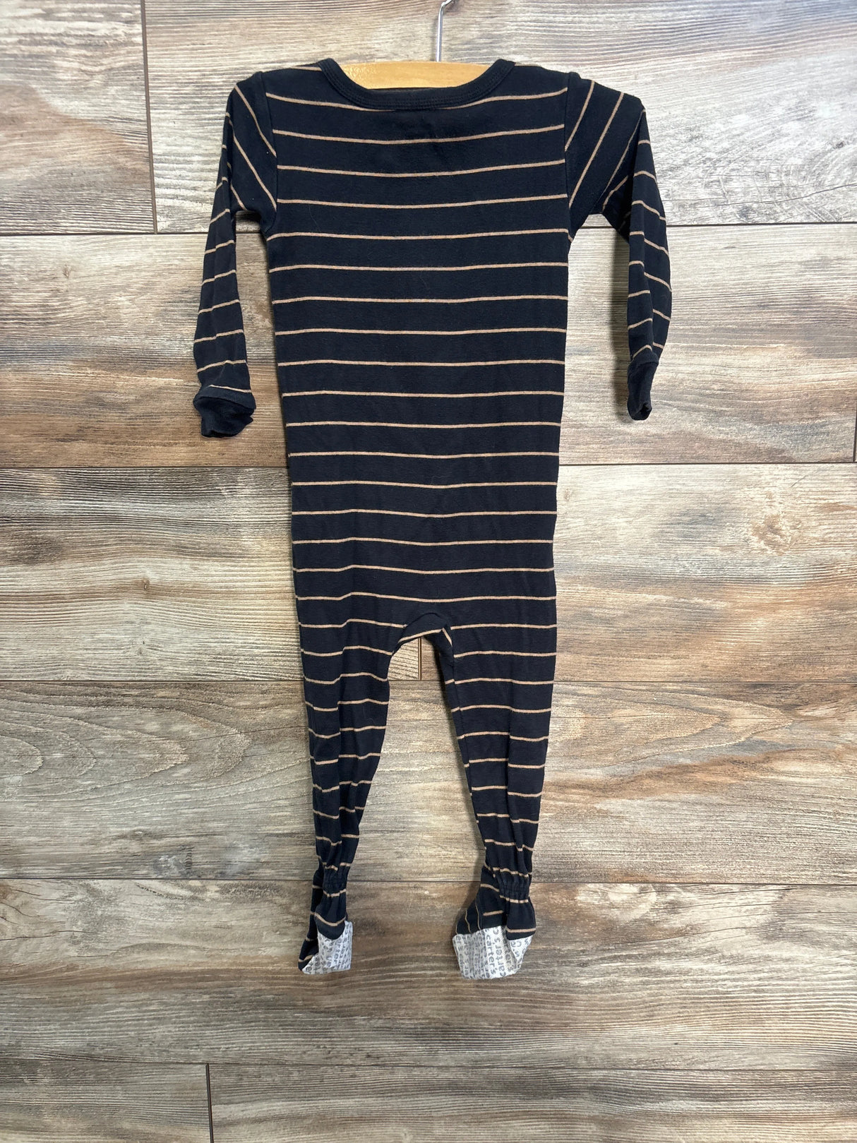 Front flat lay of black and tan striped Carter’s footed sleeper with long sleeves and gray non-slip soles on wood background