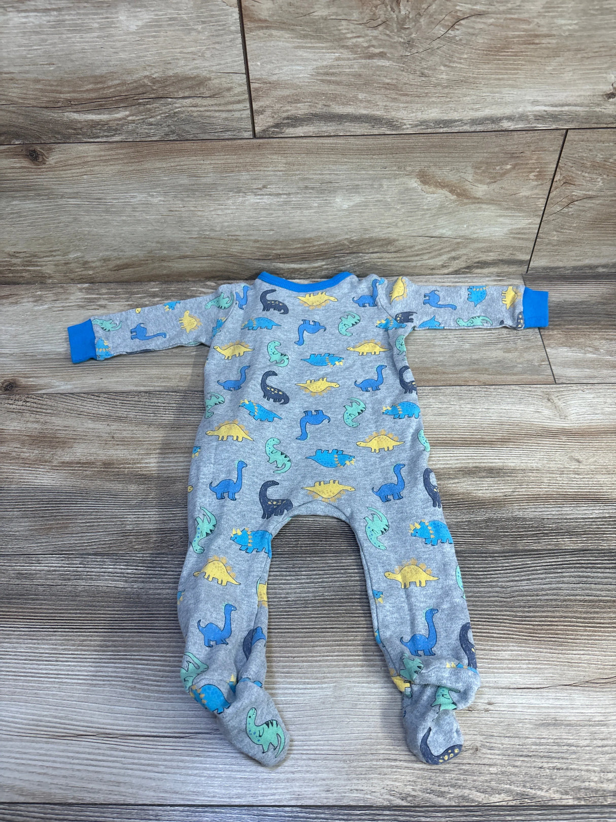 Flat lay of grey footed baby sleeper with blue cuffs and neckline, colorful dinosaur print, size 9 months on wooden background