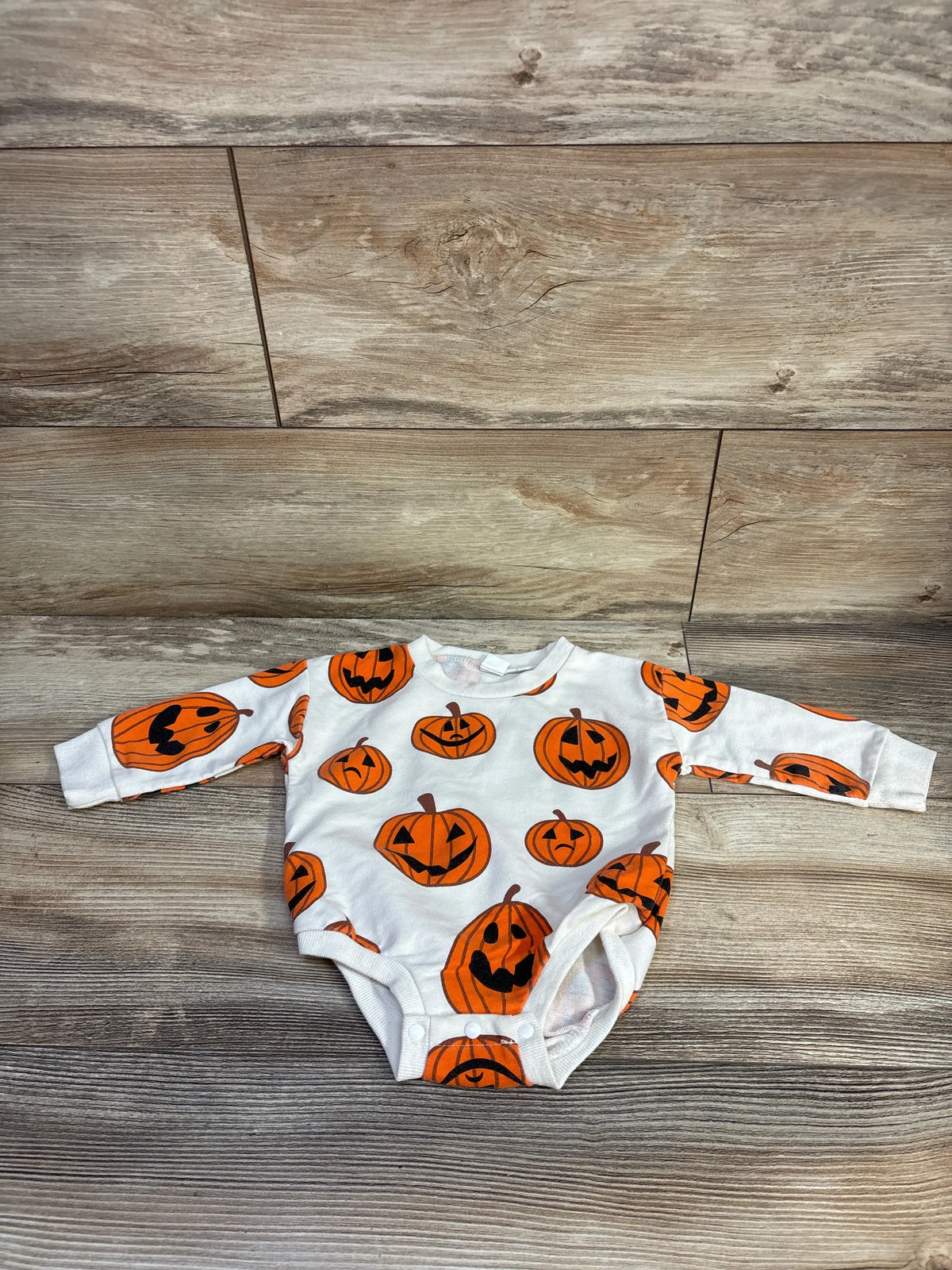 Front view of cream-colored long-sleeve bubble romper showcasing an orange pumpkin pattern with a wood-look background