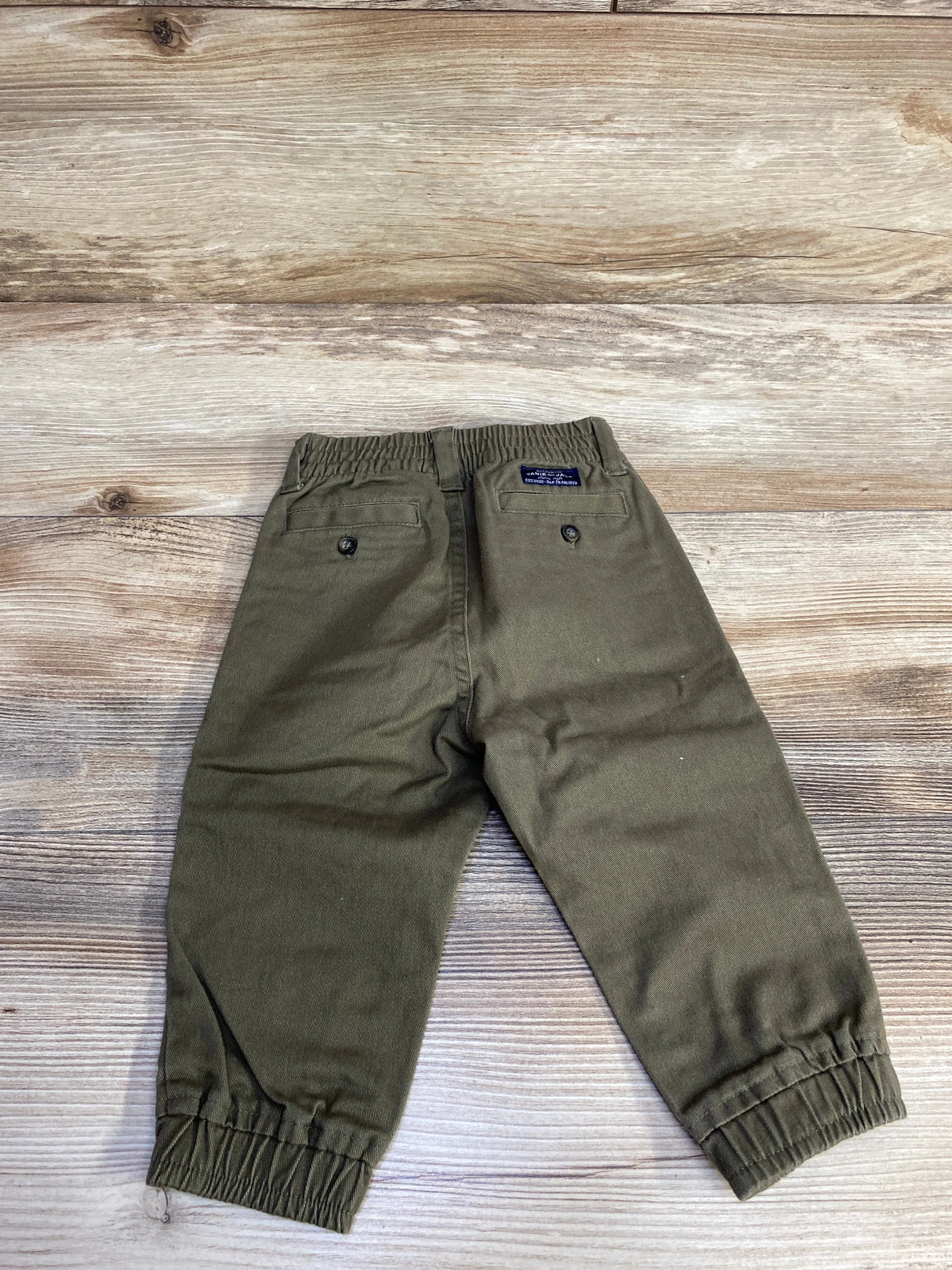 Olive green toddler pants with elastic waist and cuffs on wooden floor background