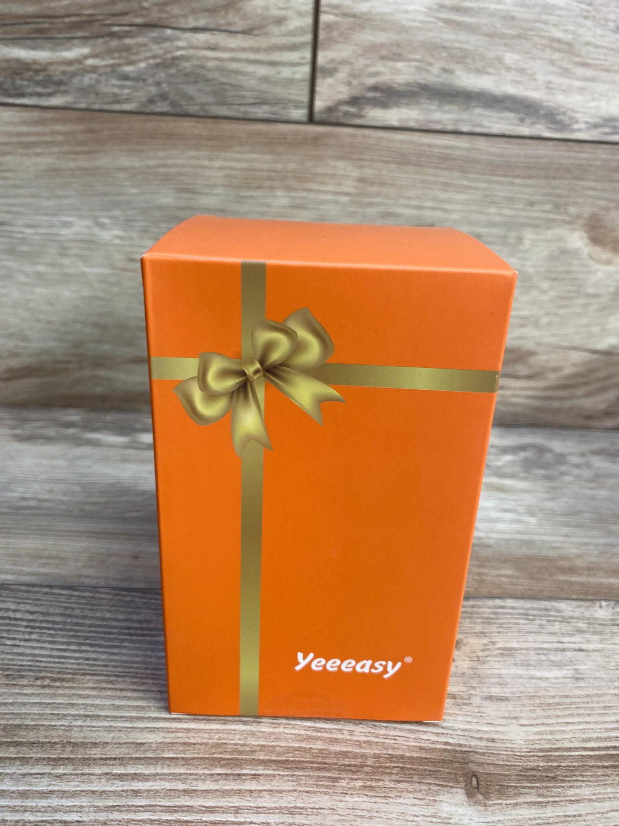 Orange Yeeeasy gift box with gold ribbon on wood background