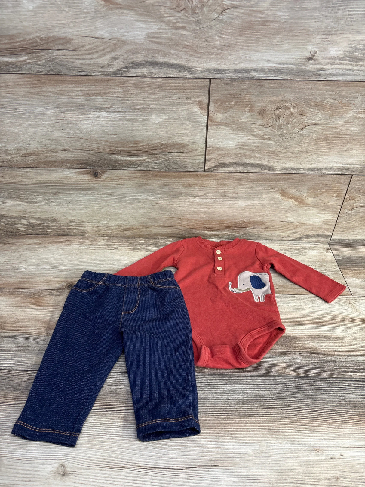 Infant outfit with red long-sleeve bodysuit featuring elephant design and dark blue pants on wood background