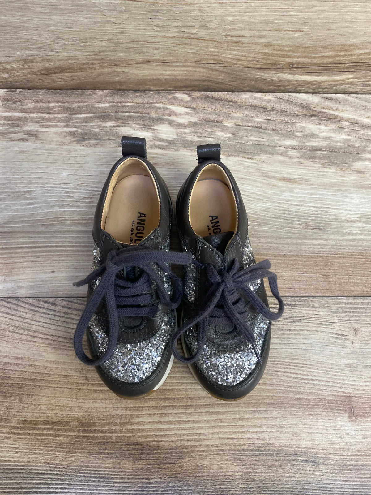 Overhead view of Angulus toddler glitter sneakers in grey showing silver glitter upper and navy laces on wood floor