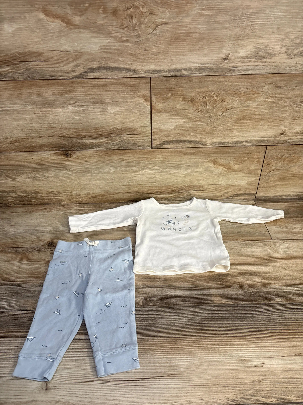 Overhead view of Carter’s two-piece baby outfit set with a white shirt reading Full of Wonder and printed pants on wood