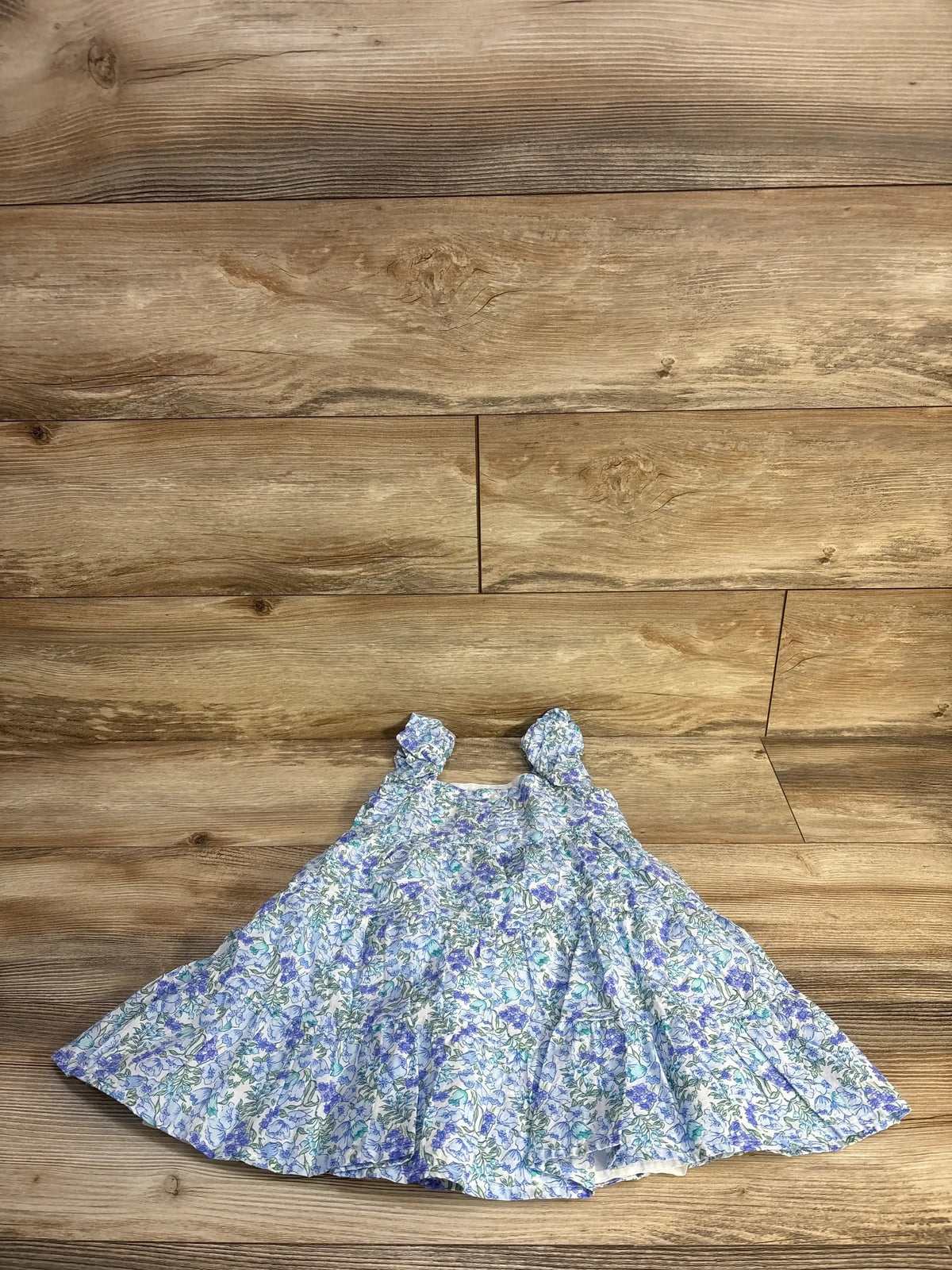 Flat lay of blue ditsy floral tiered dress size 3T with ruffle straps and tiered skirt on wood background