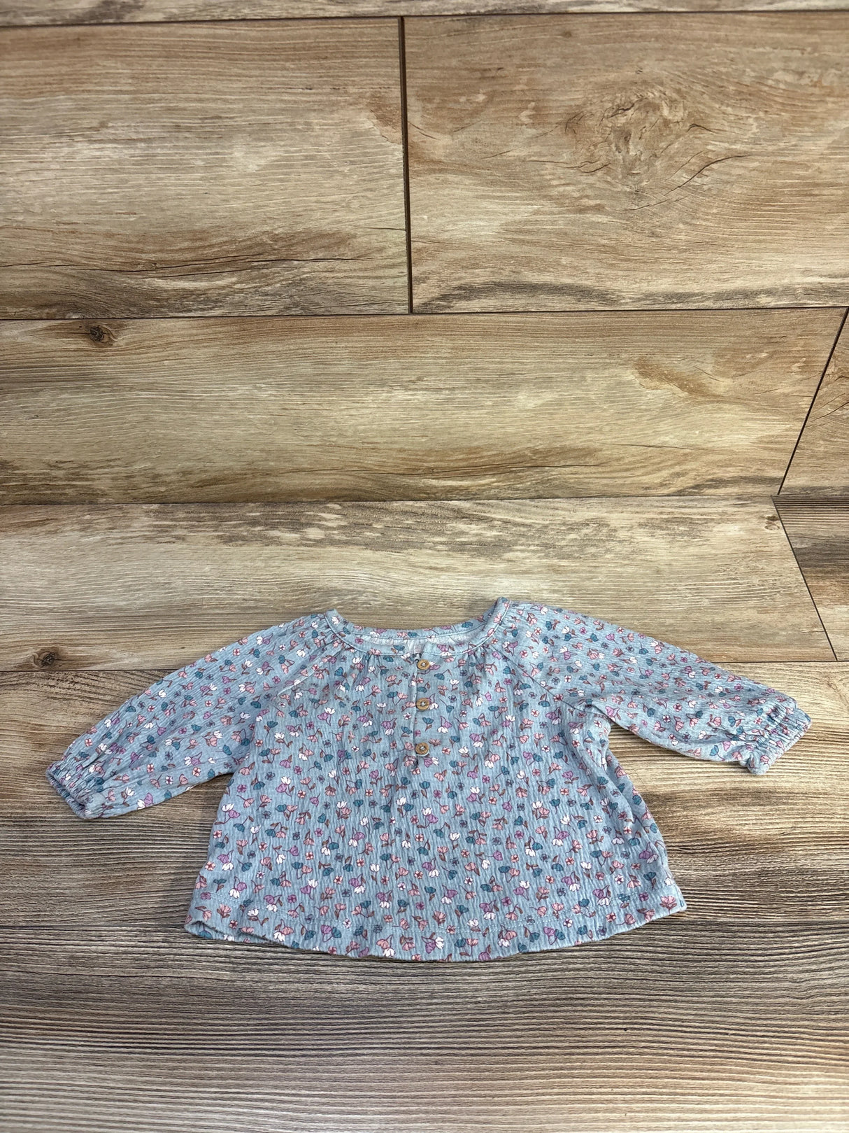 Flat lay of Carter's blue floral long-sleeve henley baby shirt showing front buttons and elastic cuffs on wood surface