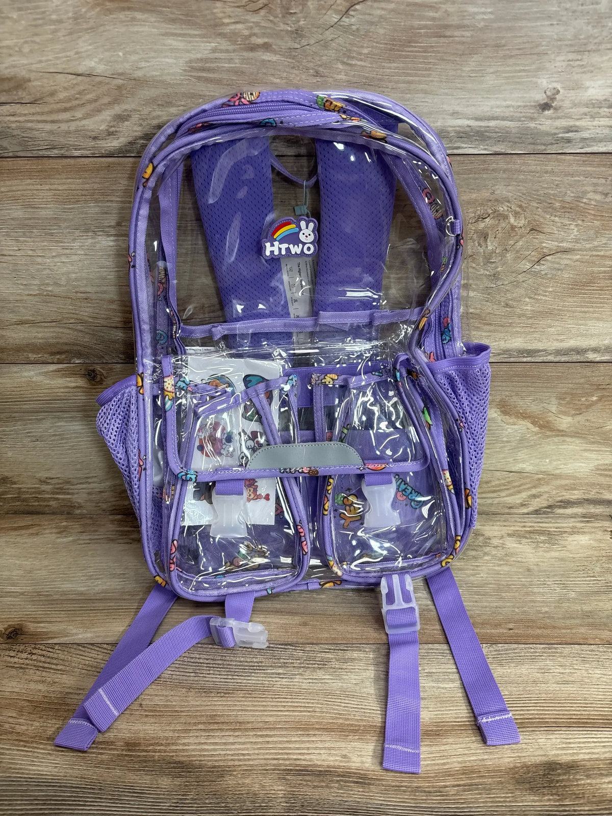 Front view of purple clear backpack showcasing multiple zippered compartments and side pockets on a wood floor