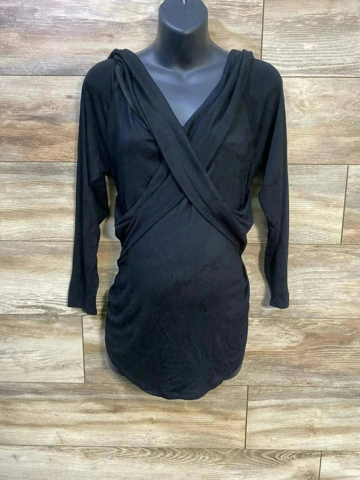 Front view of black Isabel maternity cross-front long-sleeve top on mannequin showing crossover V-neck and ruched sides against wood background