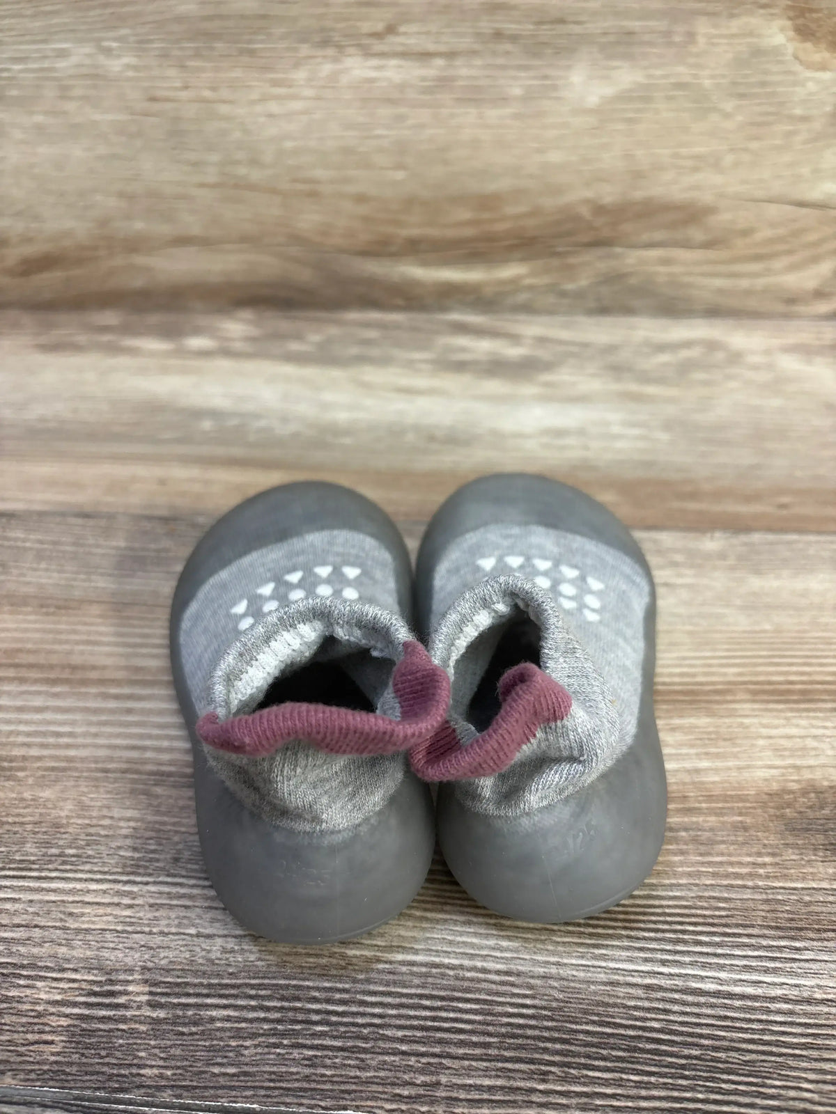 Top-down view of gray Bearbay baby sock shoes showing rubber soles and pink knit ankle pull loops on wood background