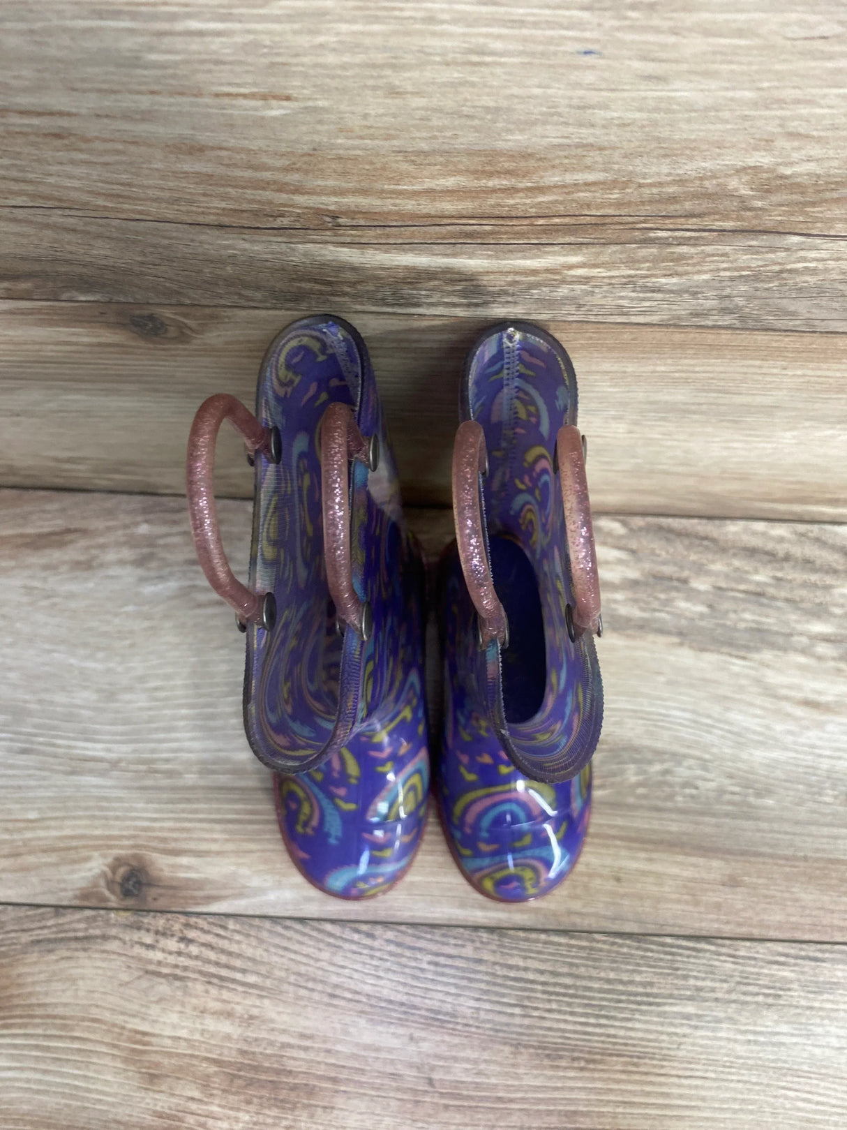 Purple paisley rain boots with pink handles on wood floor
