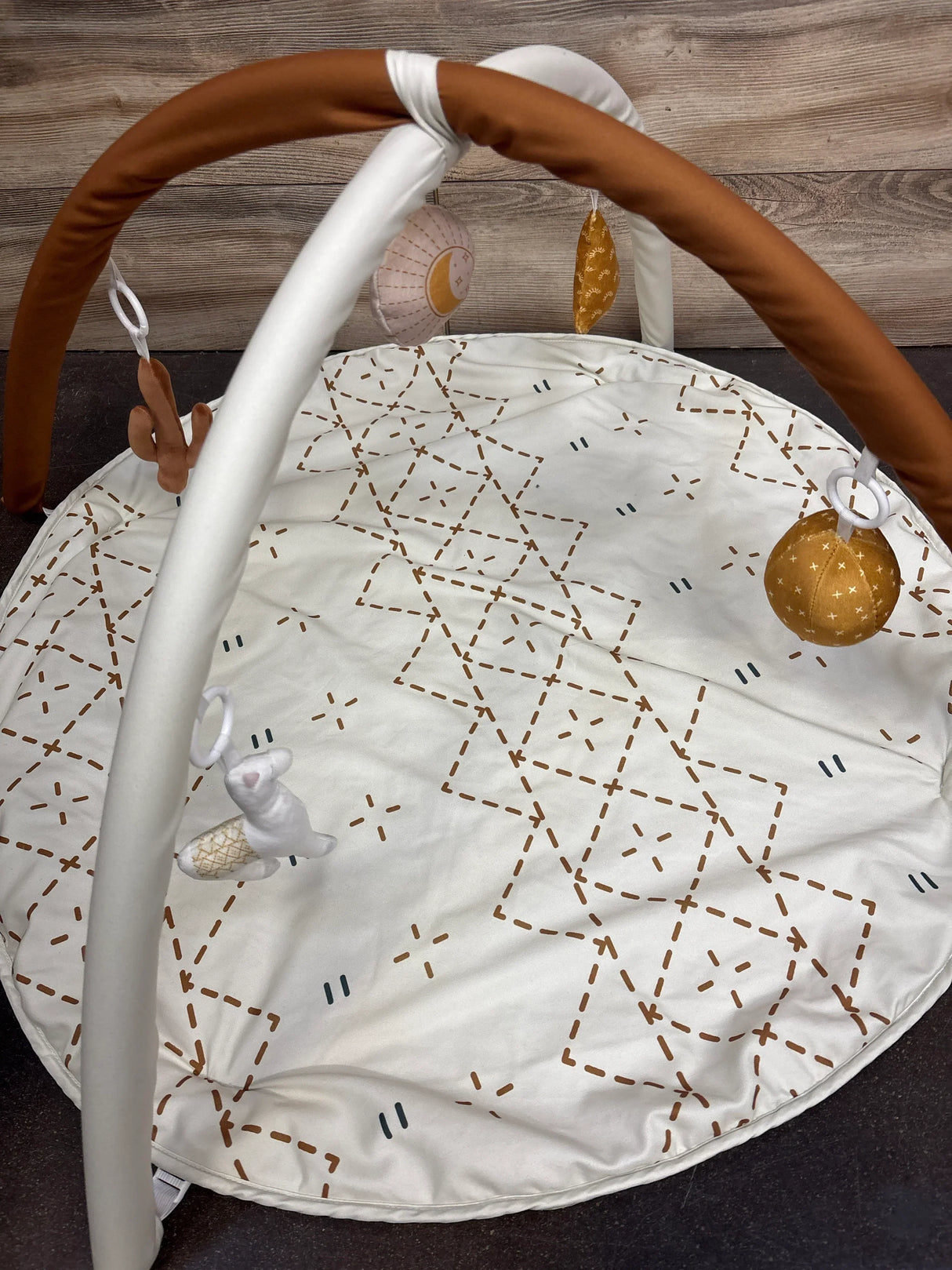 Baby play gym mat with hanging soft toys and geometric patterns on a wooden floor