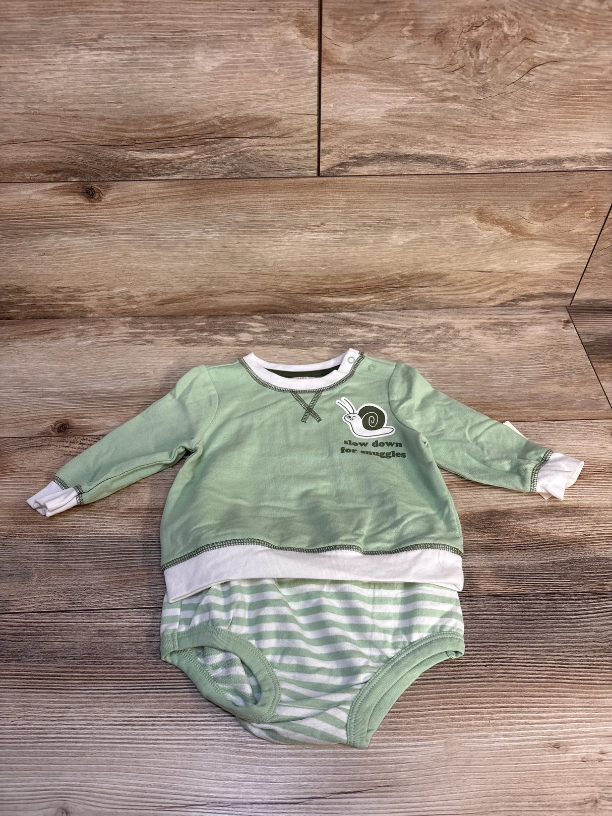 Green baby long sleeve romper with snail graphic and striped shorts on wood floor