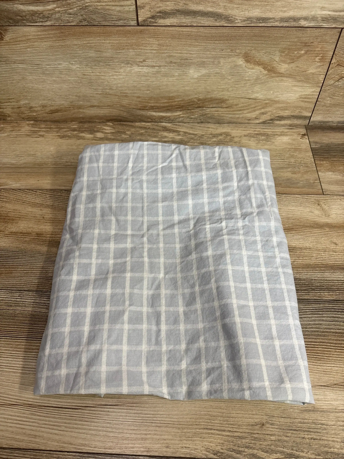Top-down view of fitted bassinet sheet showing light grey check pattern and elasticized edge on wood floor background